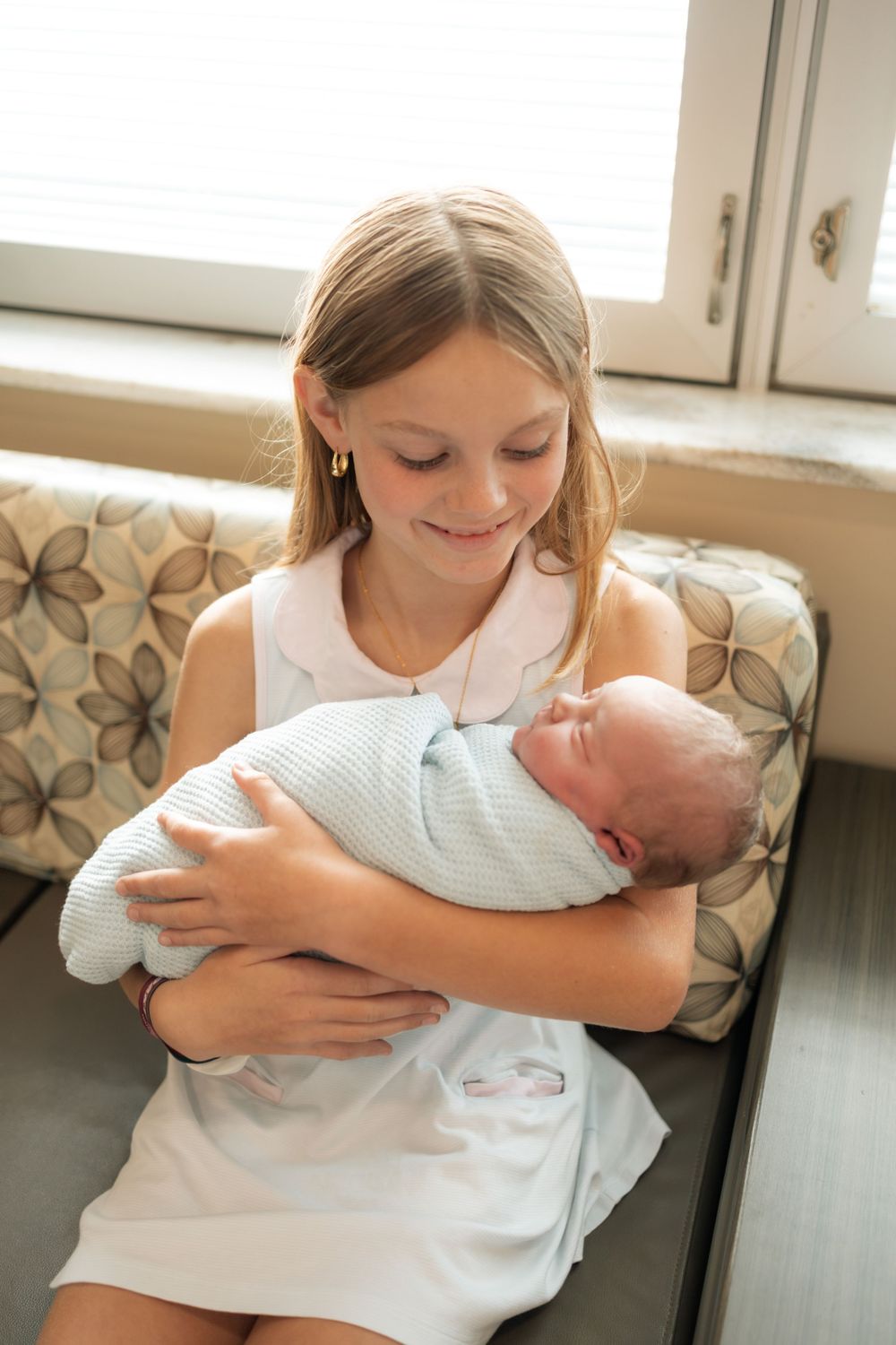 Young girl smiling while carefully holding a swaddled newborn baby in a light blue blanket indoors at Parkwest Medical Center in Knoxville.