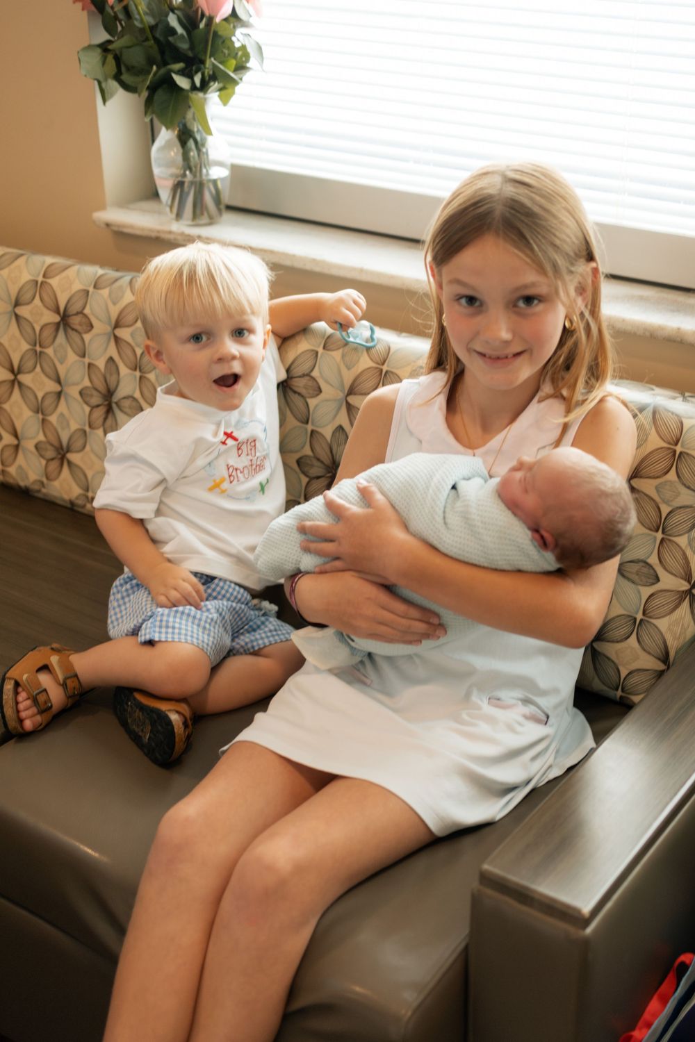 Older girl holding newborn baby on sofa with excited toddler at Parkwest Medical Center in Knoxville, TN.