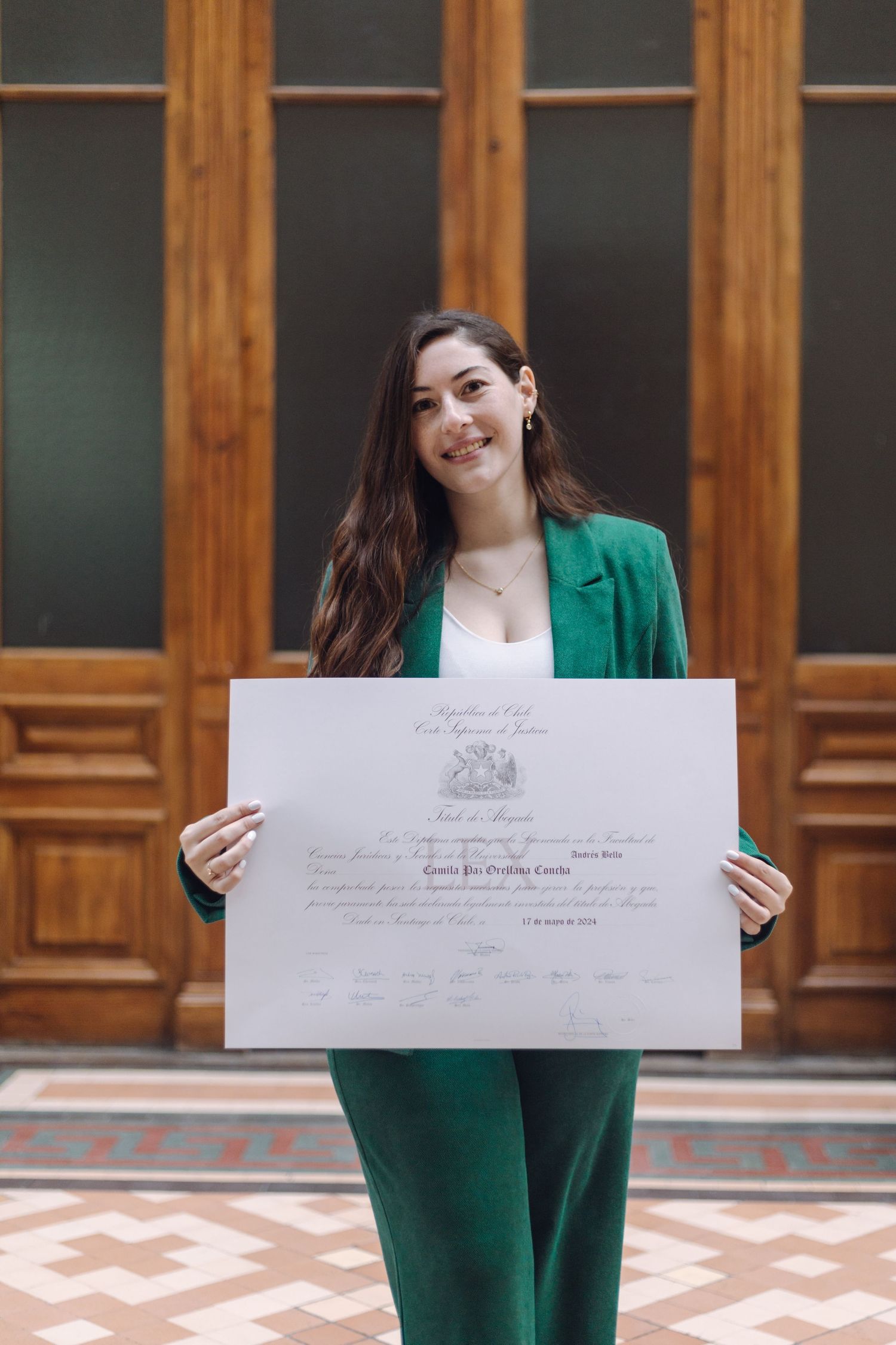 Young woman in green blazer holding official Chilean court certificate before wooden doors.
