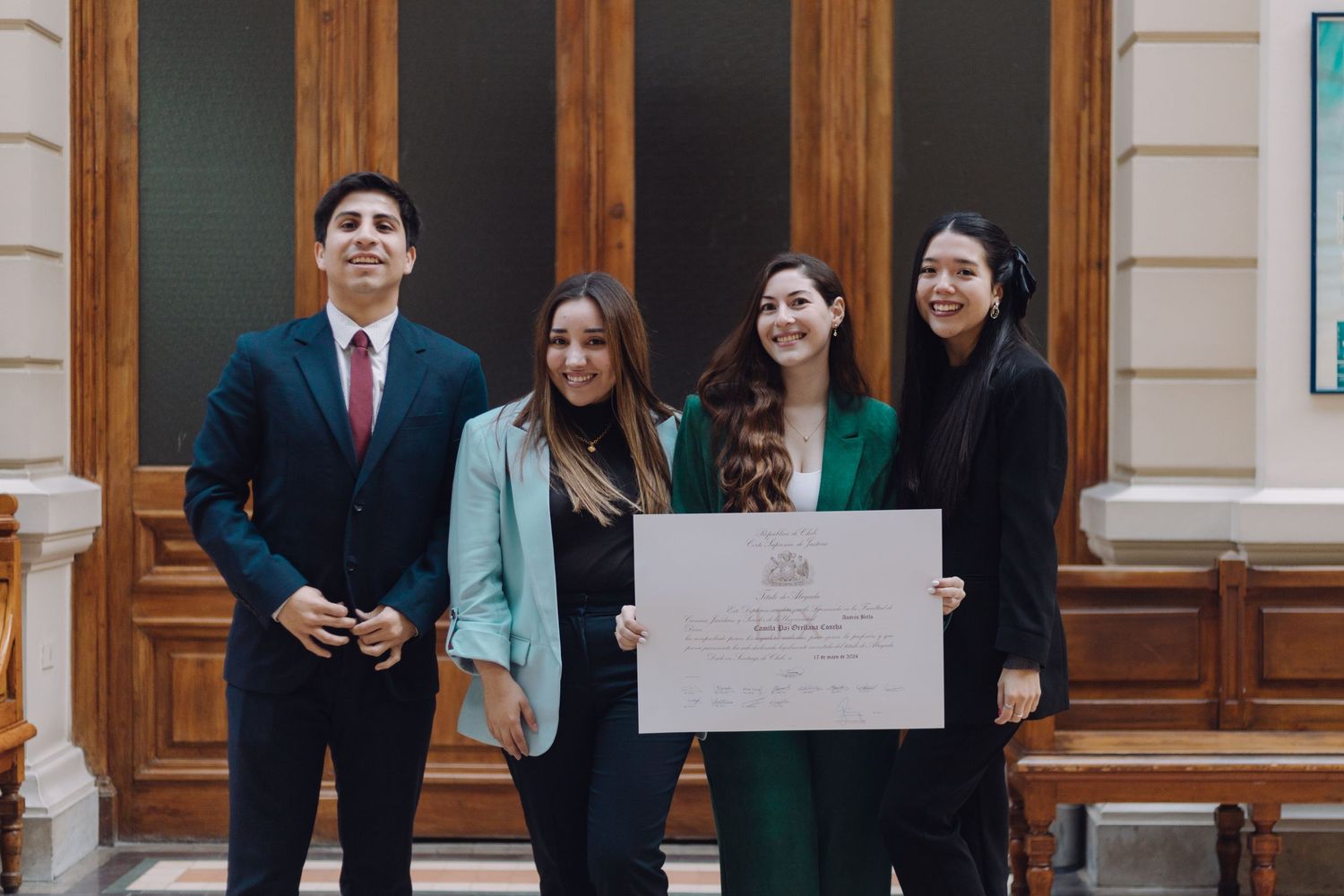 Four young graduates pose proudly with diploma in elegant academic building.