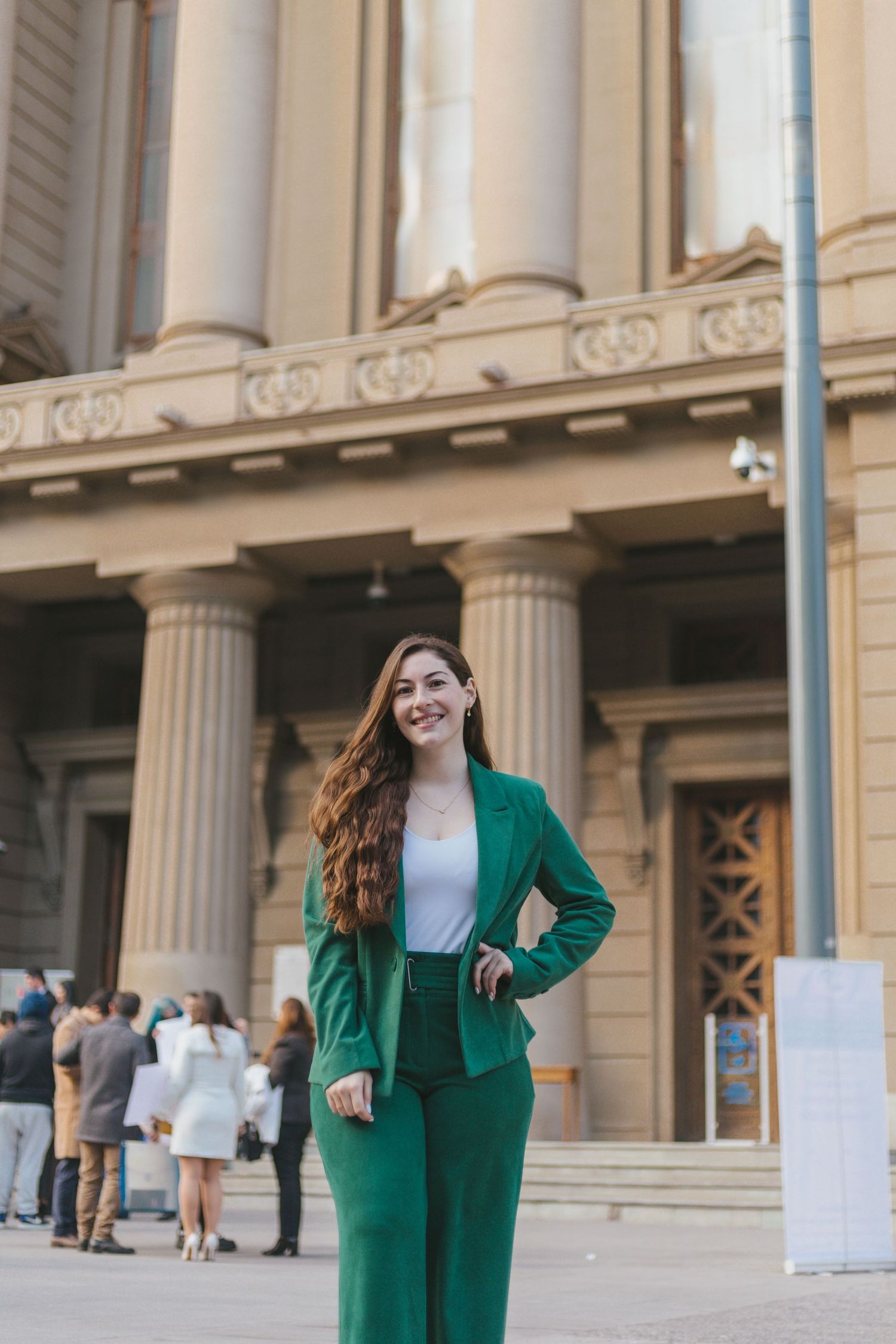 Elegant young woman in green suit poses outside grand neoclassical building exterior.