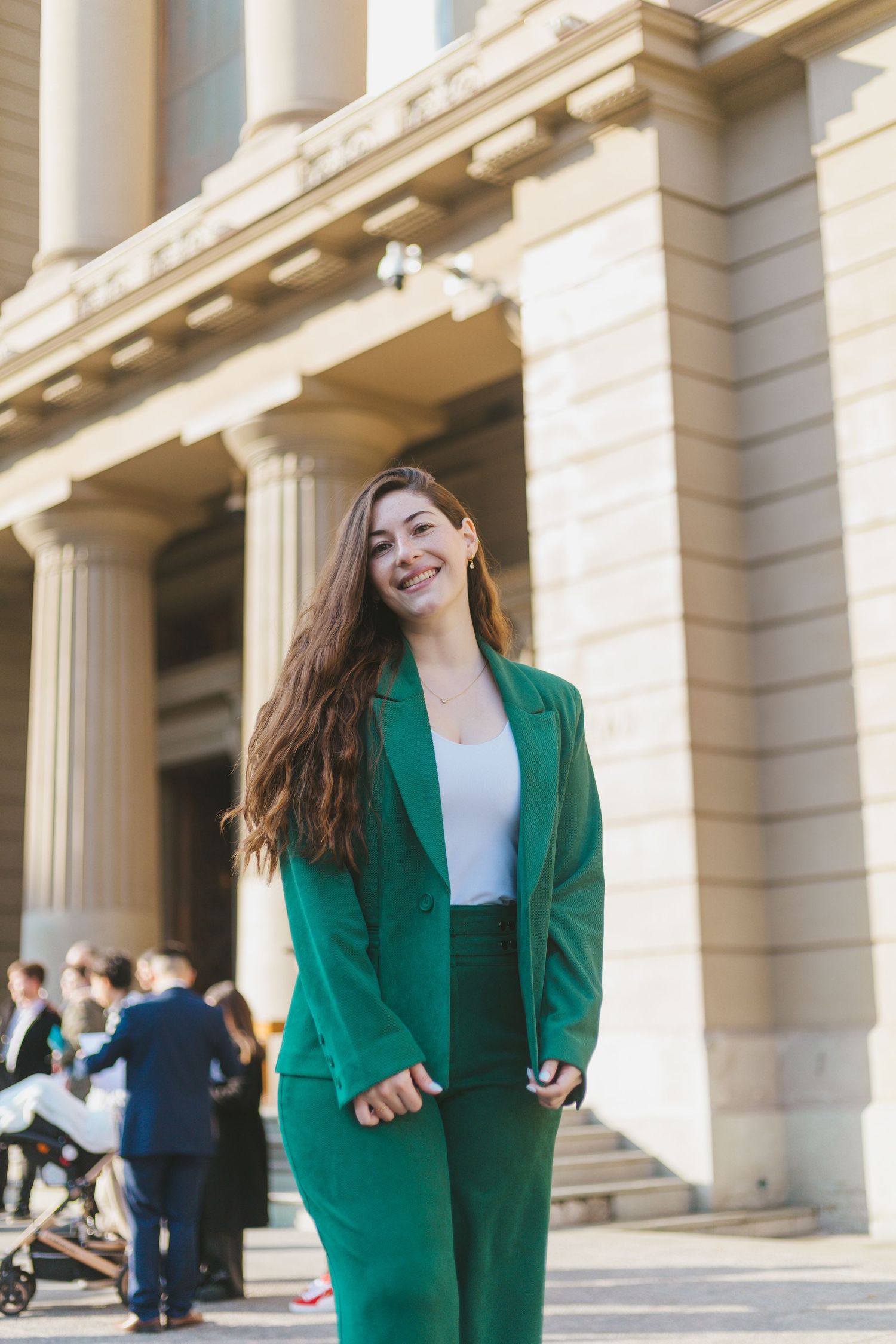 Young woman in green pantsuit smiling confidently outside a classical building with columns.