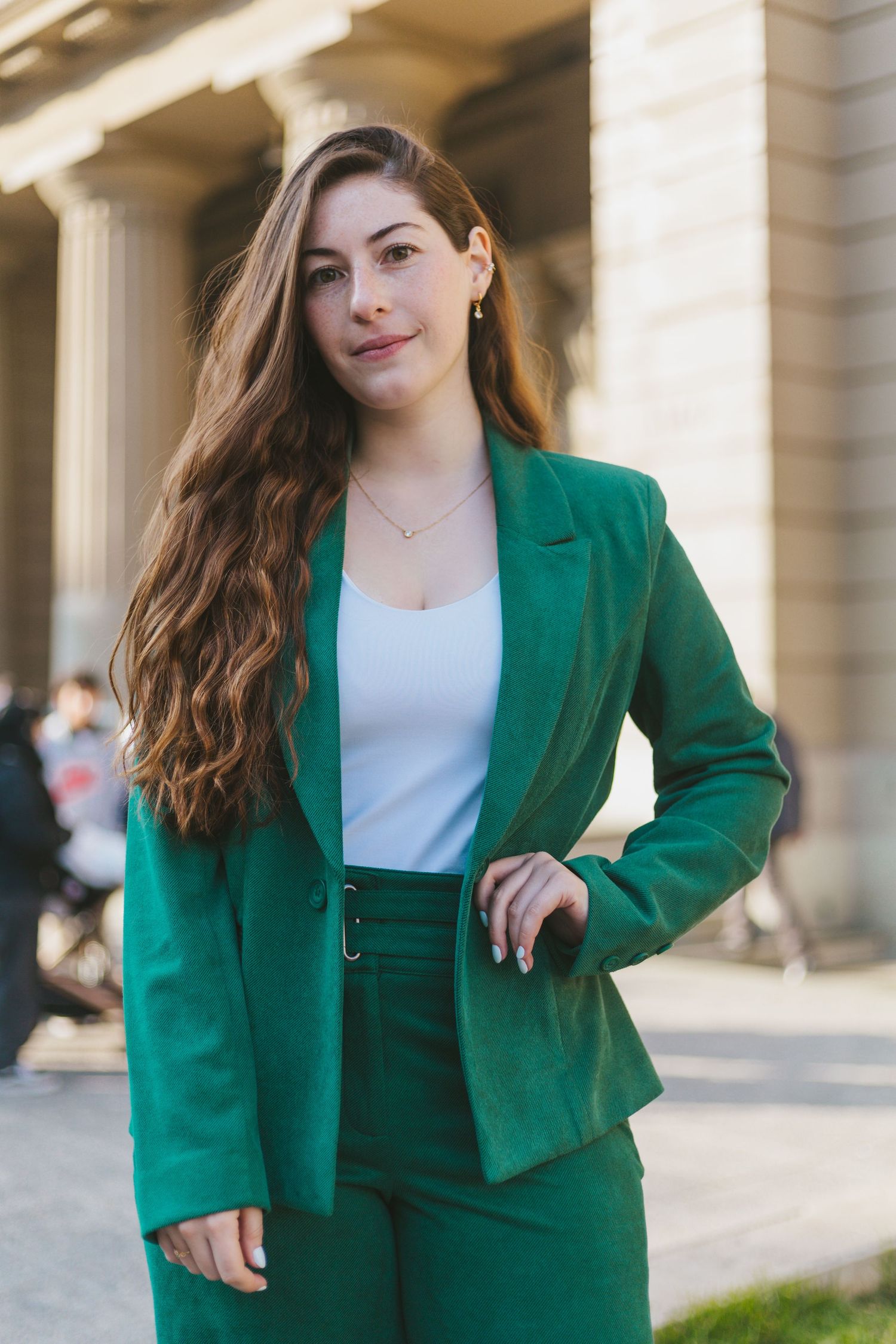 Elegant young woman in green blazer and pants posing outside a classical stone building.