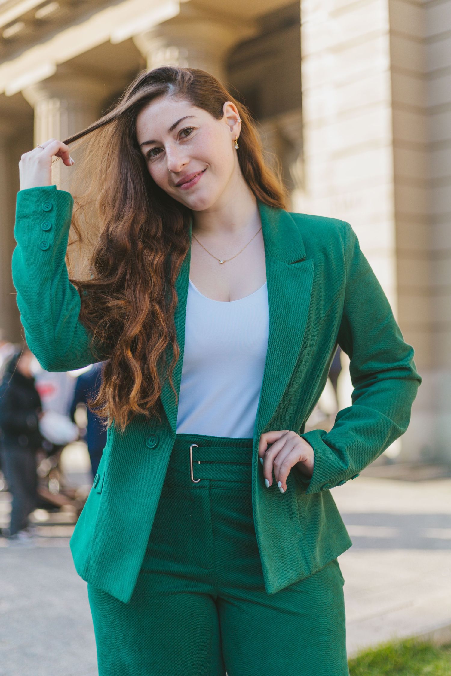 Stylish young woman in green suit playing with her hair outside a historic building.