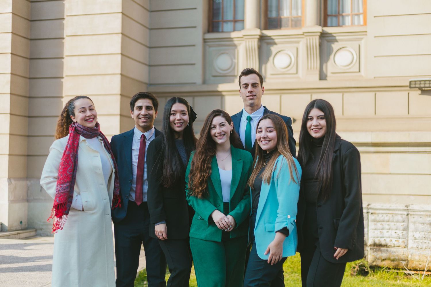 Group of seven young professionals posing together outside a historic building.