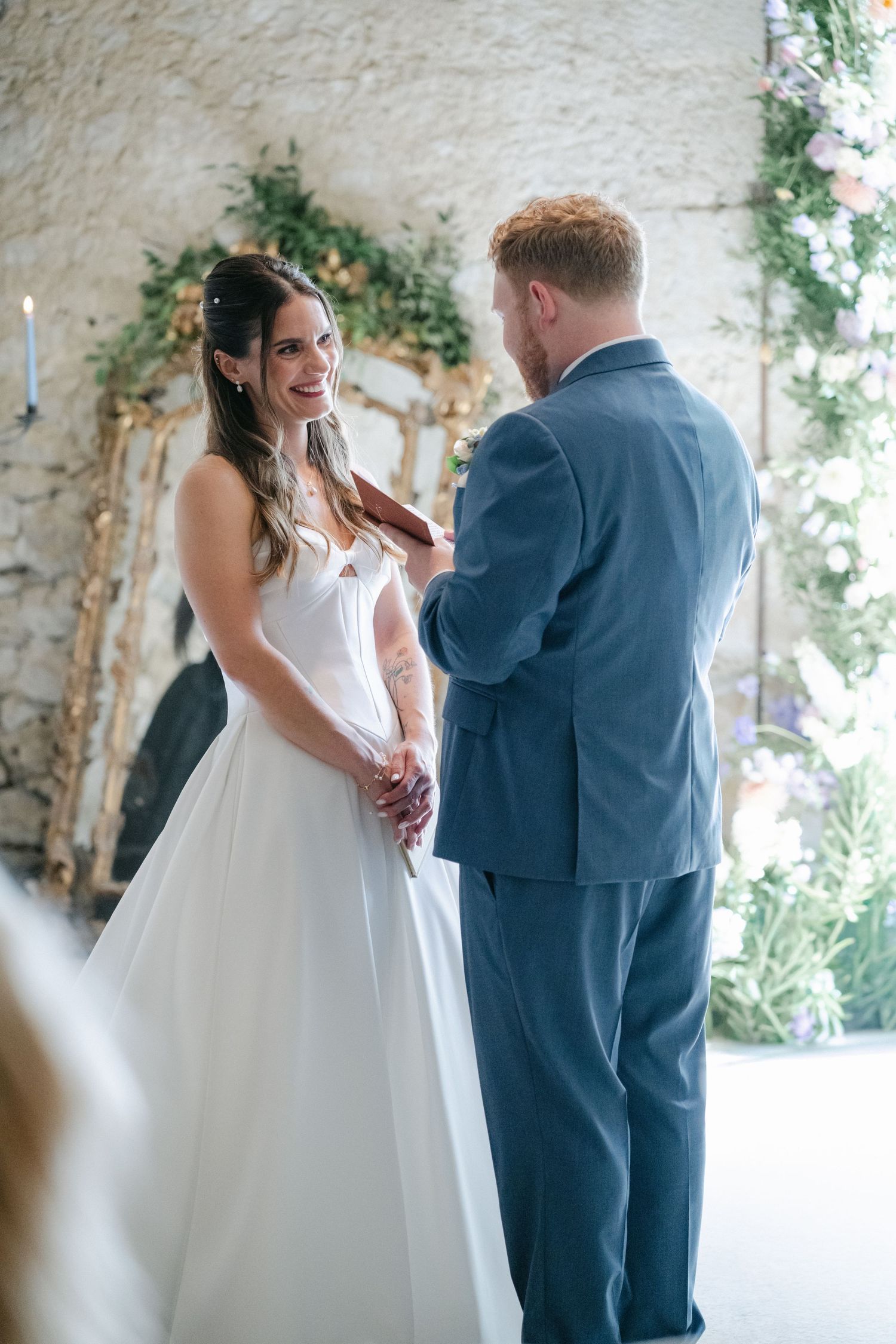 Bride and groom exchange vows in a stunning stone arch venue adorned with floral arrangements and soft natural light.