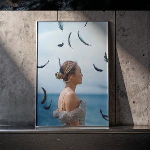 Artistic framed portrait of a woman in profile with feathers falling against a moody ocean sky backdrop.