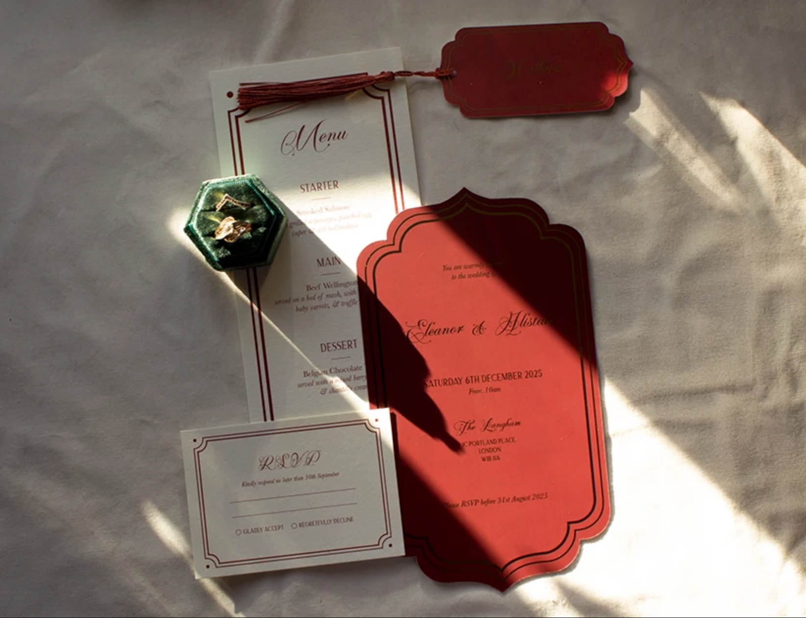 Red acrylic wedding invitation suite with menu and RSVP card on white fabric.