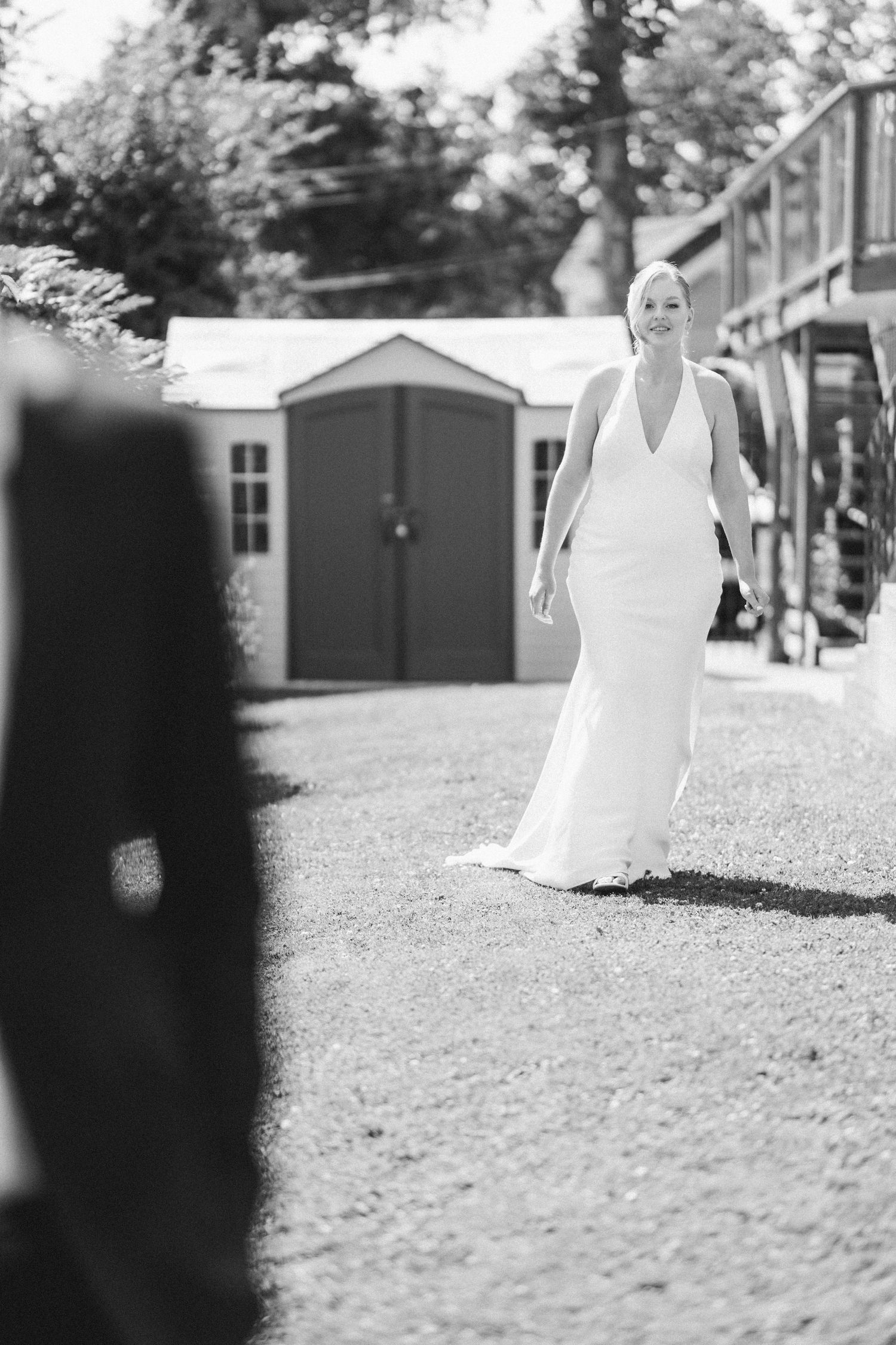 Bride in elegant white halter gown walking toward groom during outdoor first look at wedding venue.