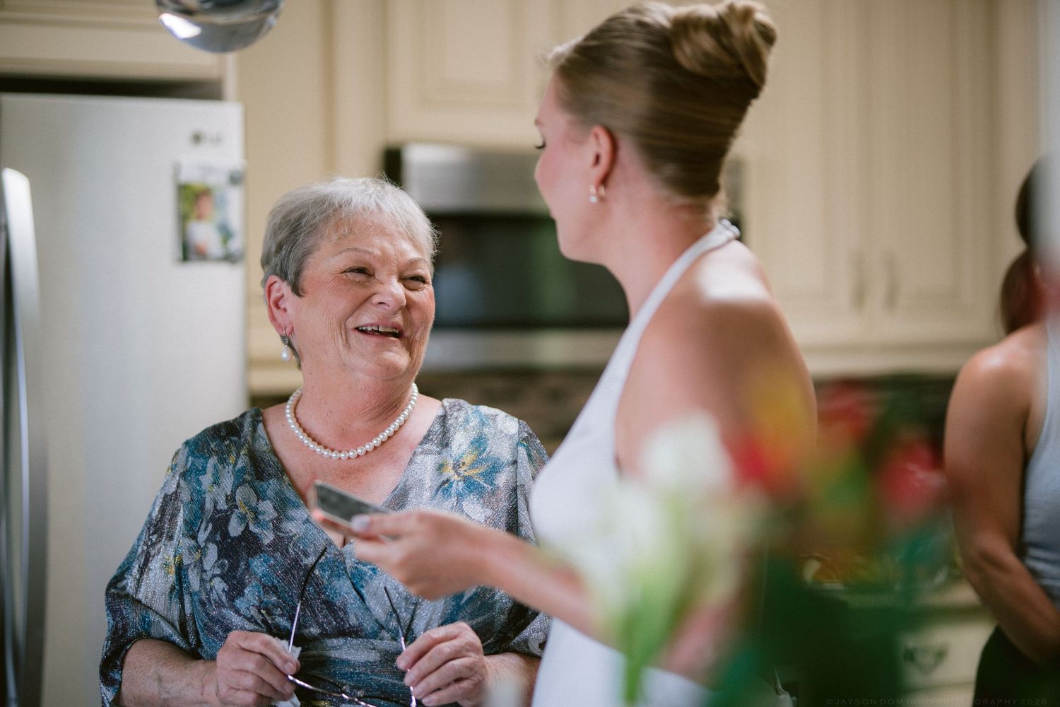 Joyful grandmother in blue floral dress shares warm moment with bride holding colorful bouquet.
