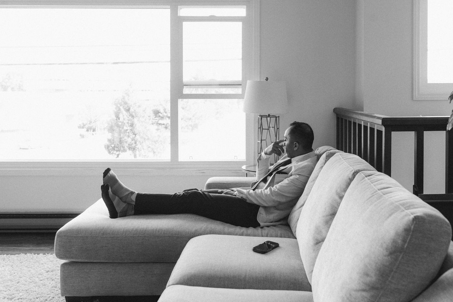 Groom relaxing on a sectional sofa in black and white photo before wedding ceremony.