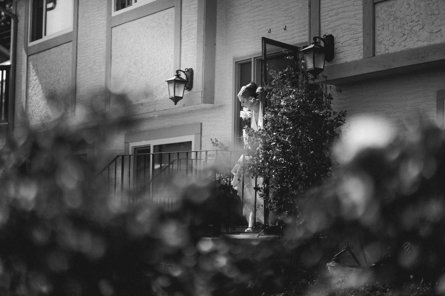 Black and white photo of bride in wedding gown standing at doorway of elegant venue entrance.