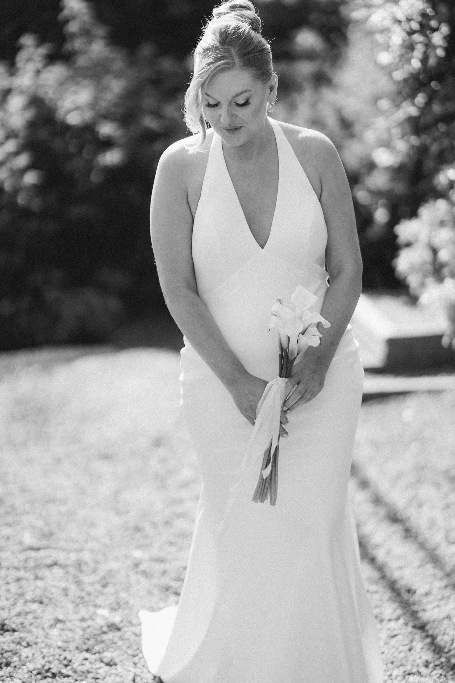 Bride in white halter gown holding calla lily bouquet in black and white outdoor portrait.