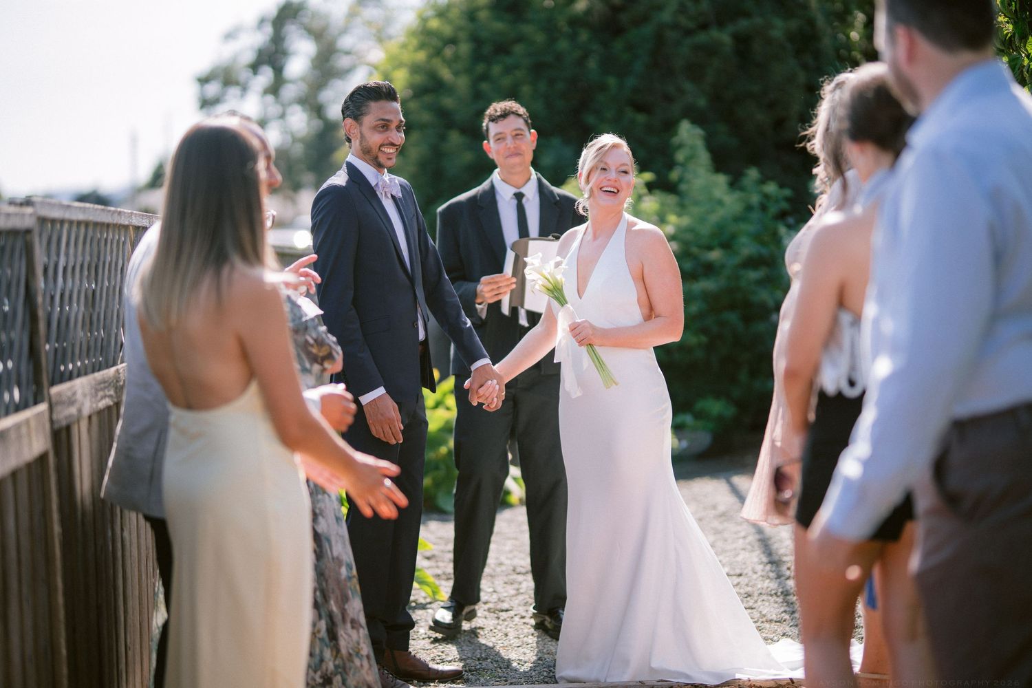 Newlywed couple celebrates with wedding guests in a sunny garden after their outdoor ceremony.