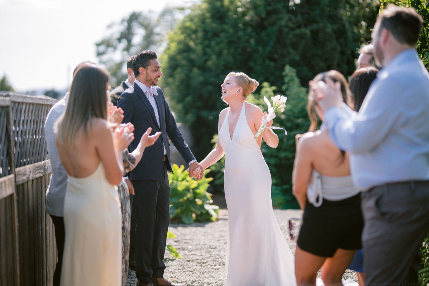 Newlywed couple celebrating with guests after outdoor wedding ceremony on sunny summer day.