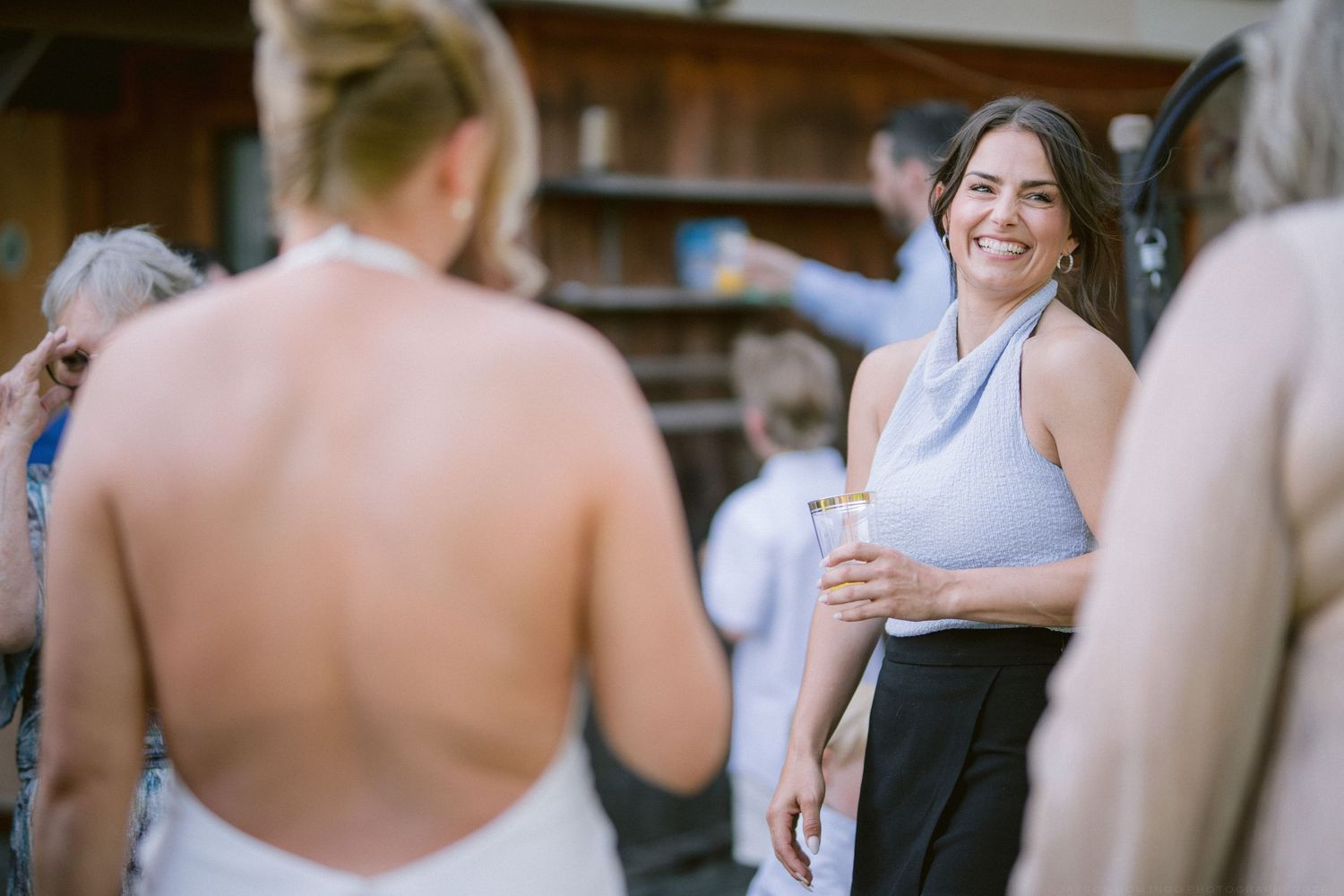 Smiling bridesmaid in blue halter top holding champagne glass at outdoor wedding reception.