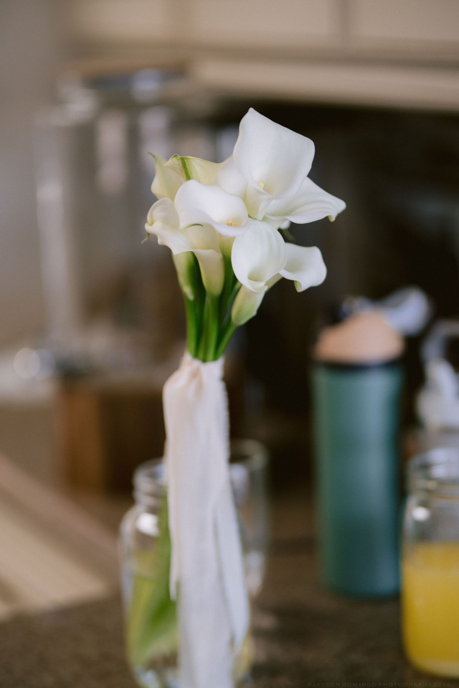 White calla lily bridal bouquet tied with ribbon displayed in glass jar vase.
