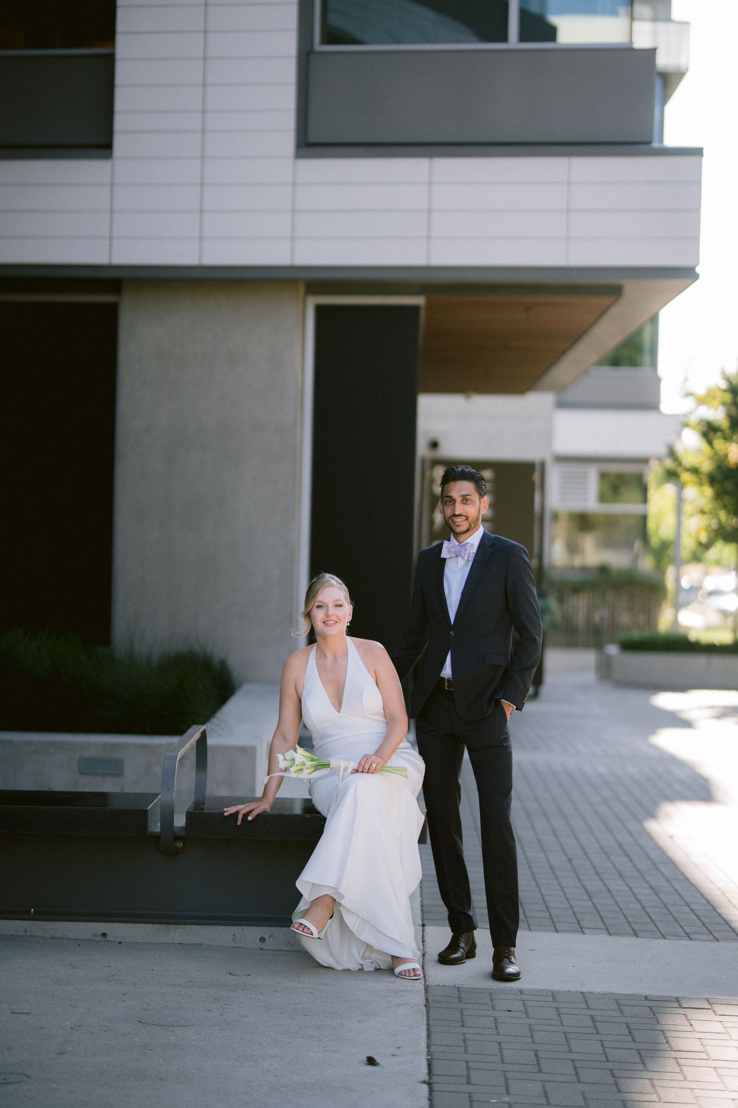 Smiling bride and groom posing outside a modern building on their wedding day.