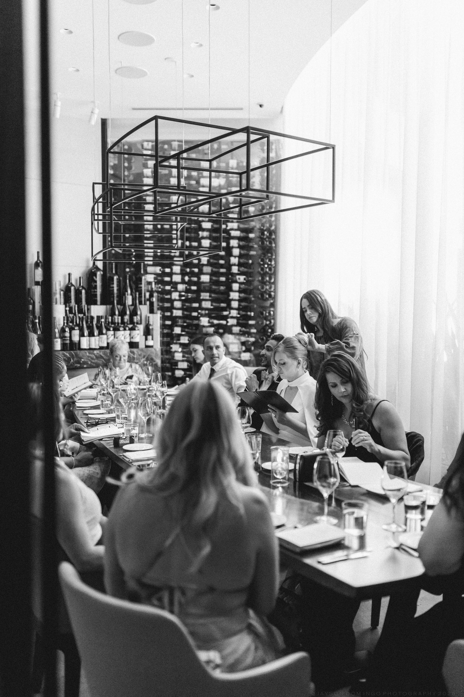 Black and white photo of elegant wedding reception dinner at upscale restaurant with wine display.