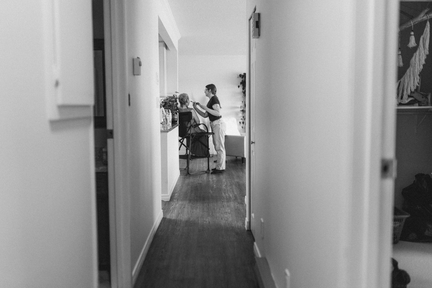 Black and white photo of bride getting hair done in a hallway before the wedding ceremony.