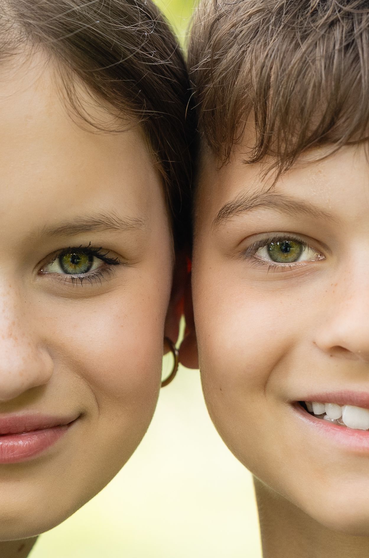 Close-up portrait of two children with striking green eyes smiling together outdoors.