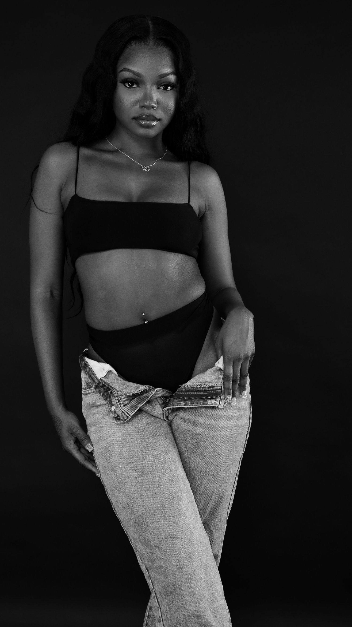 Black and white studio photo of woman in black crop top and denim jeans.