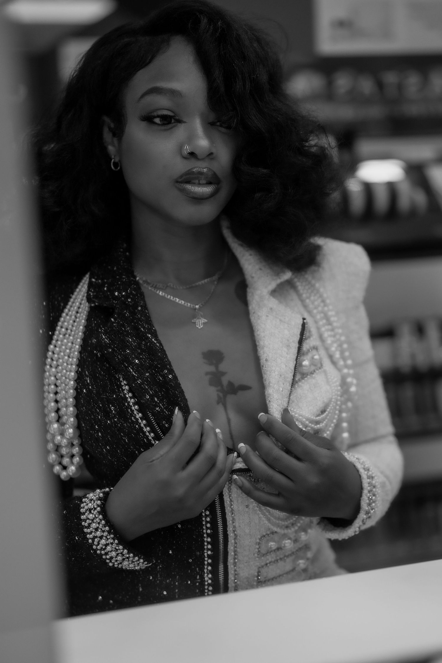 Black and white close-up of a woman in pearl necklaces and sequined outfit touching her chest.
