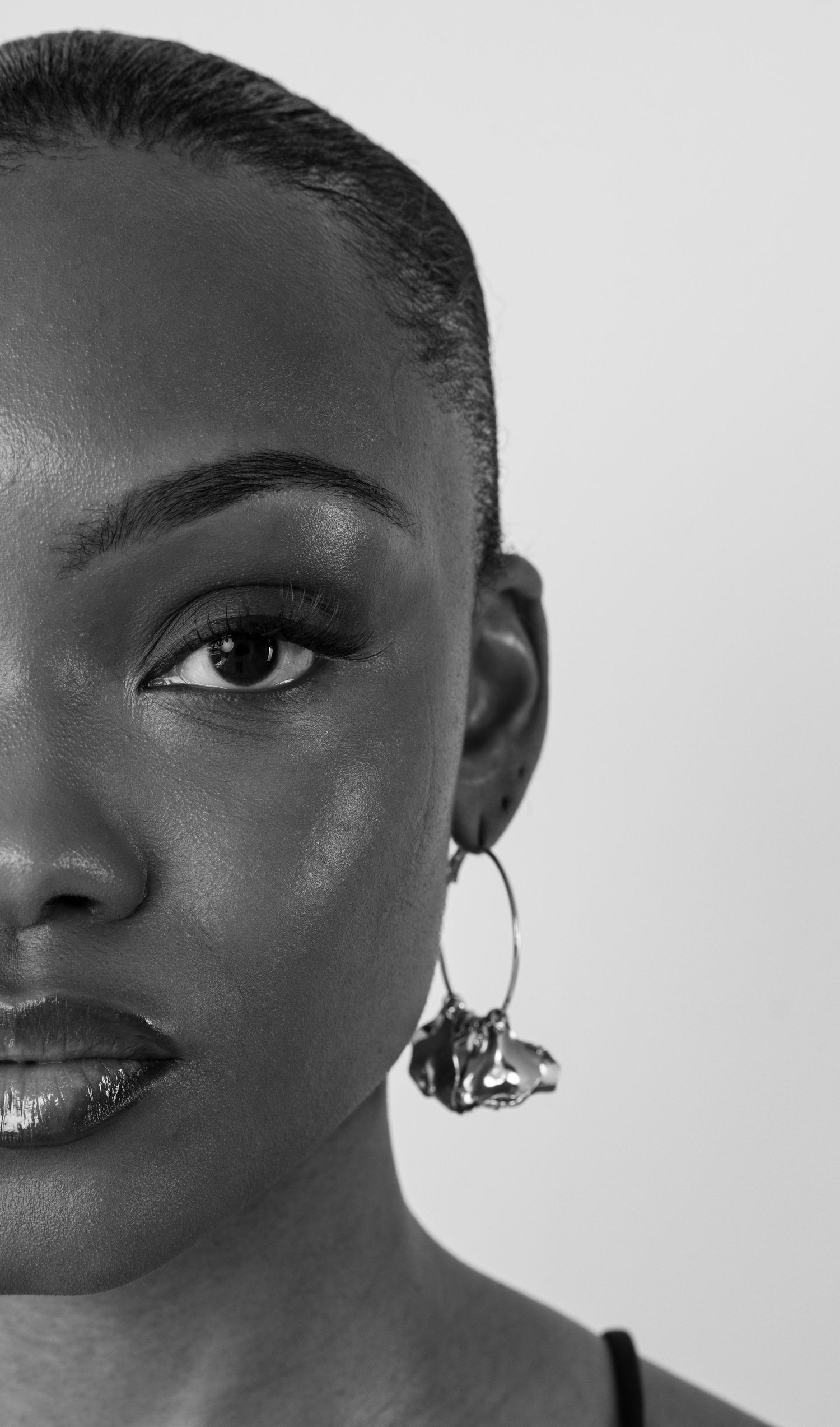 Black and white close-up portrait of a woman wearing a decorative hoop earring with bold eye makeup.