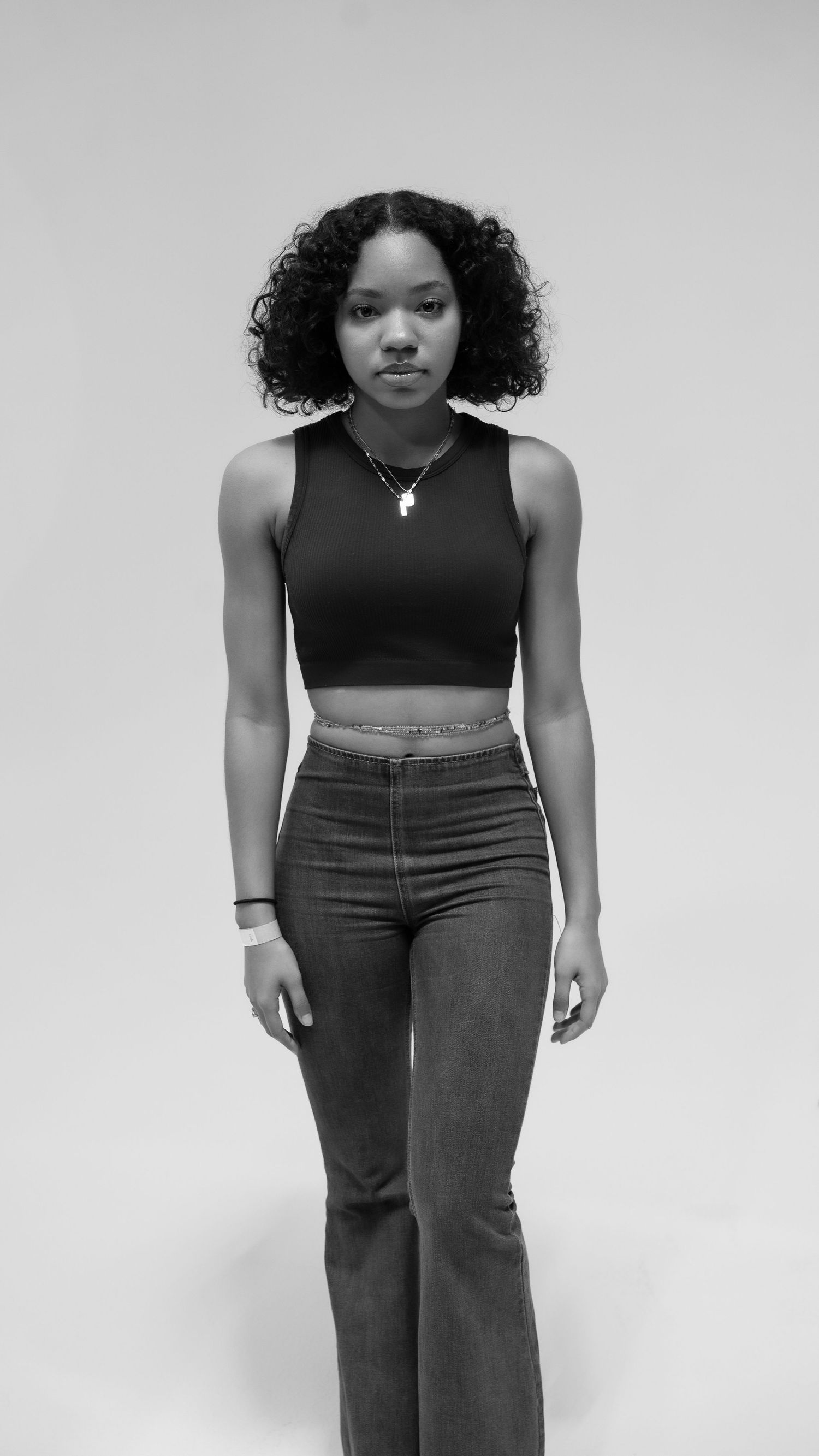 Black and white photo of a young woman in a crop top and high-waisted flare jeans posing against a light background.