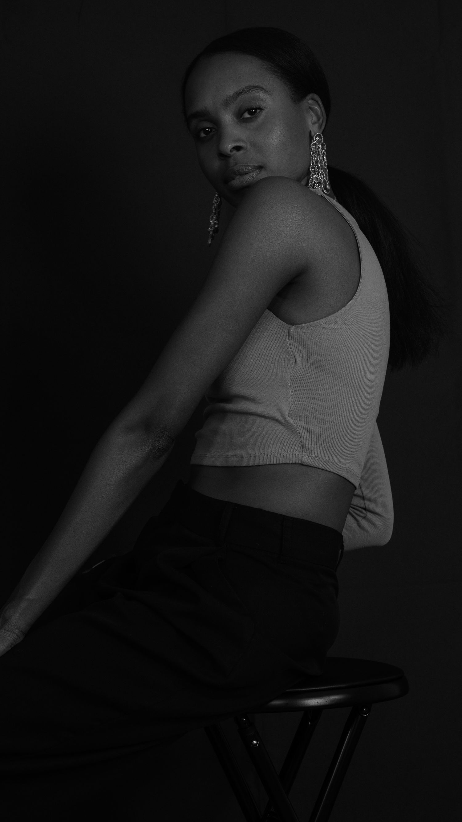 Black and white studio photo of a woman in a crop top and black skirt seated on a stool.