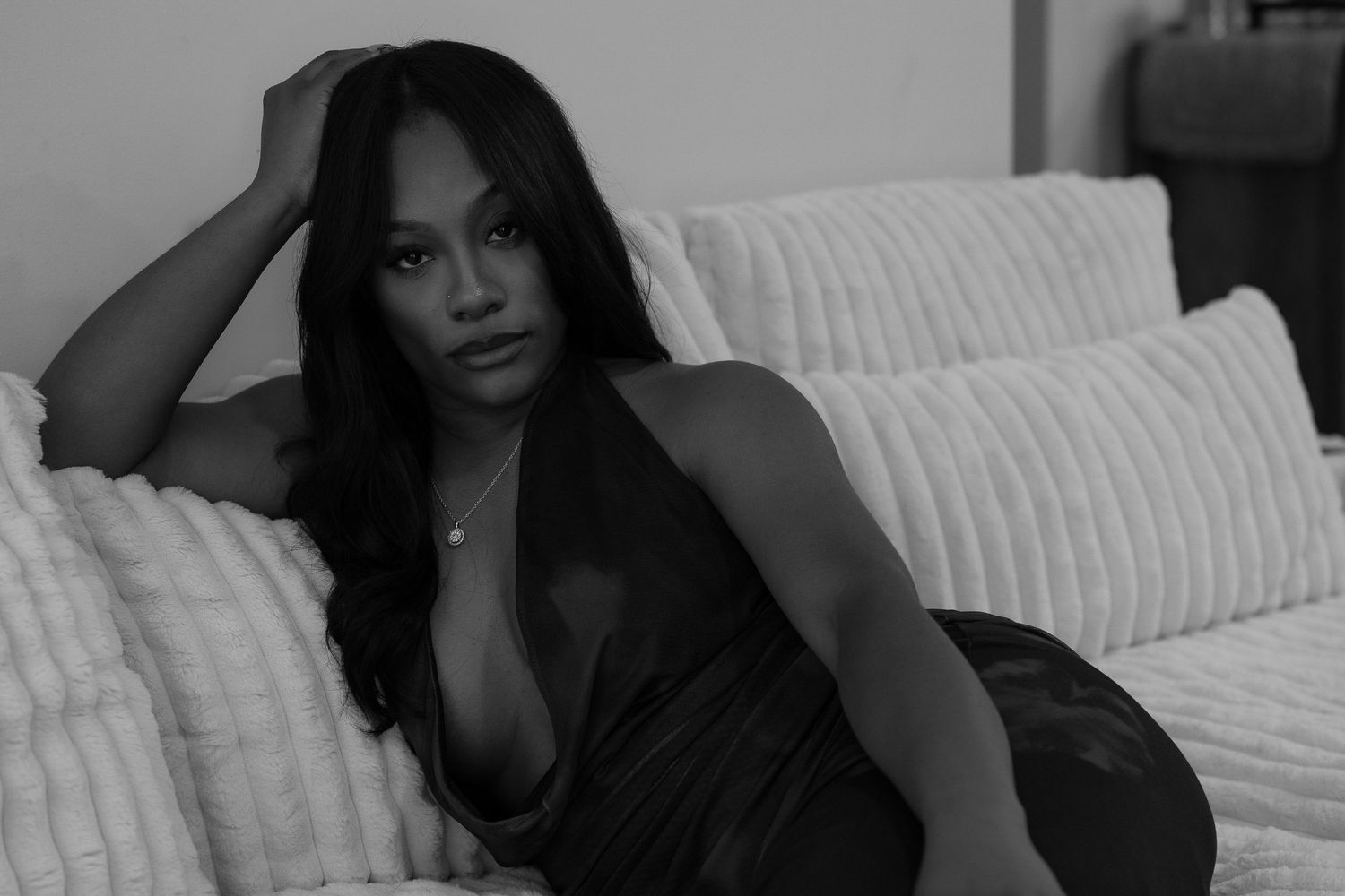 Black and white photo of a woman in a dark dress posing elegantly on a white couch.