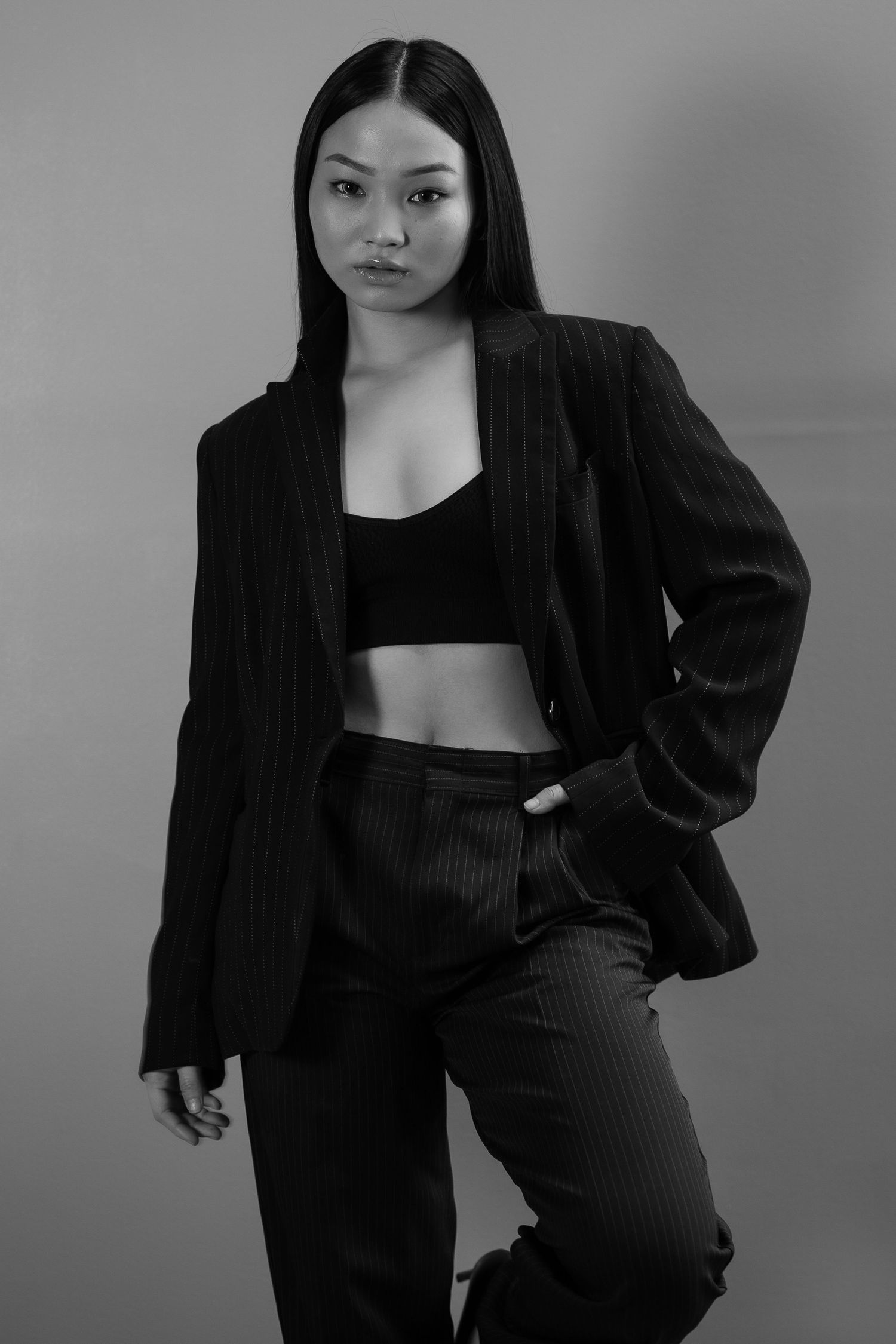 Black and white studio portrait of a woman in a pinstripe blazer and crop top posing confidently.