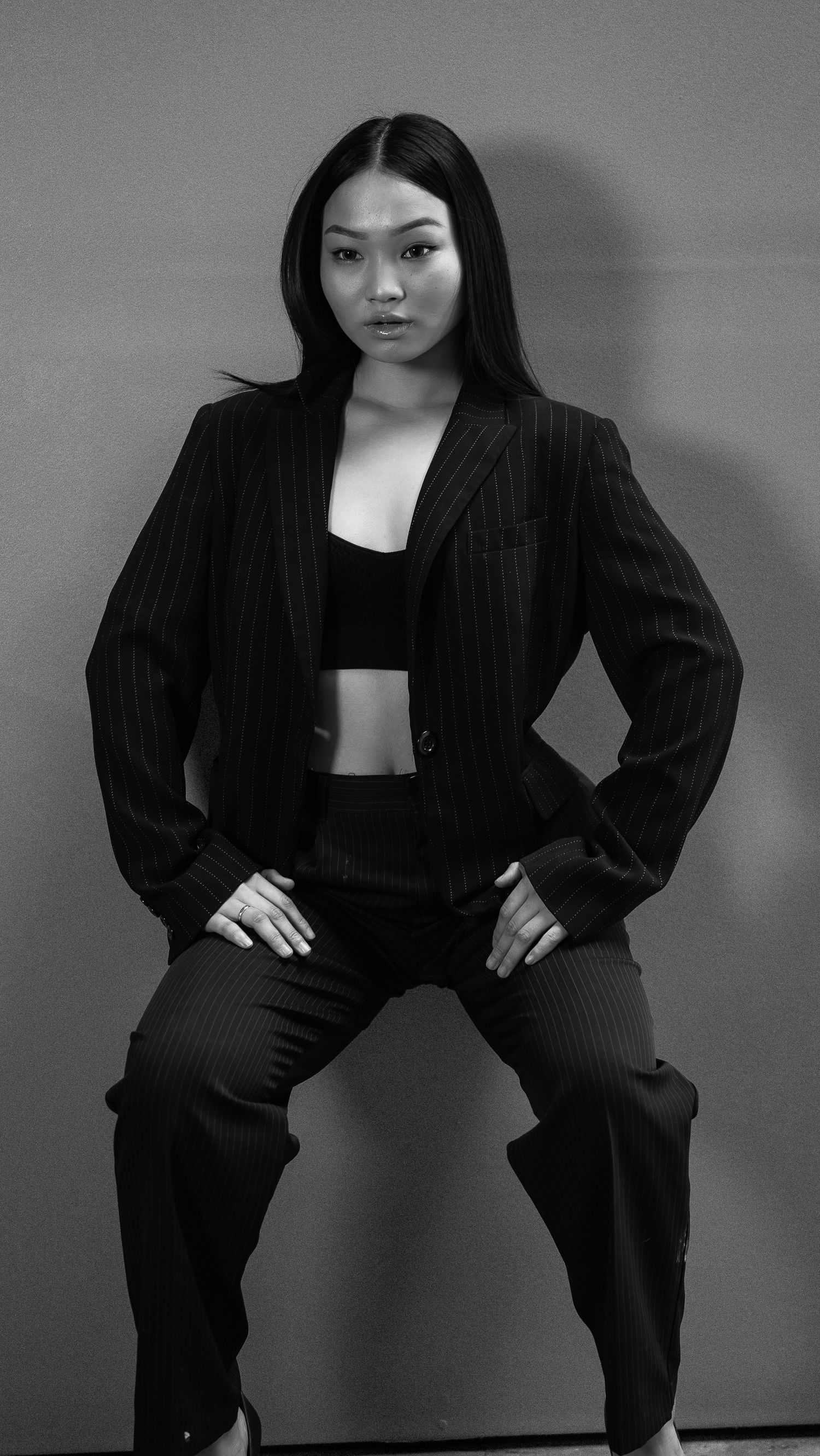 Black and white photo of a young Asian woman posing confidently in a pinstripe blazer and crop top.