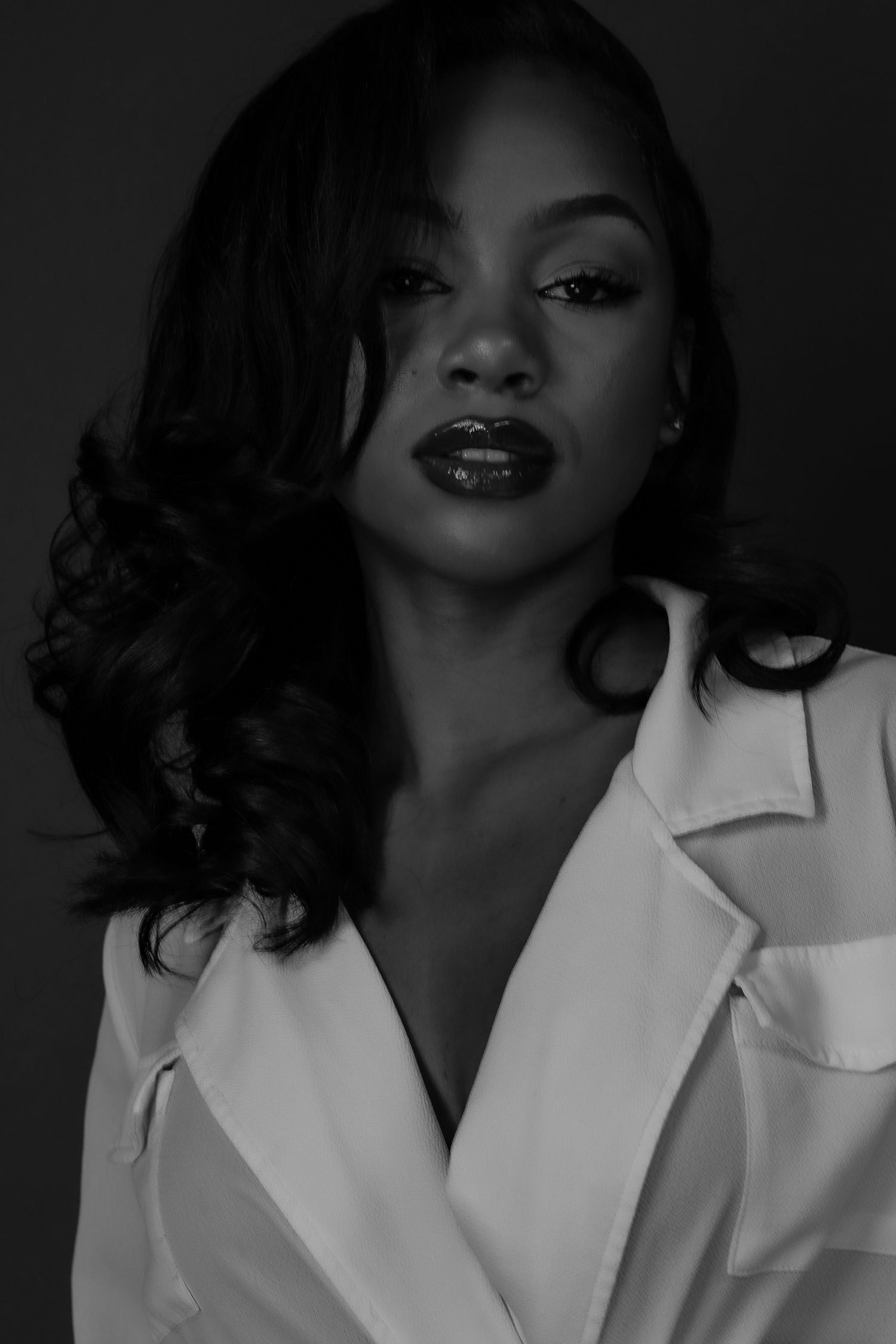 Black and white dramatic close-up portrait of a woman in a white blazer with bold lips.