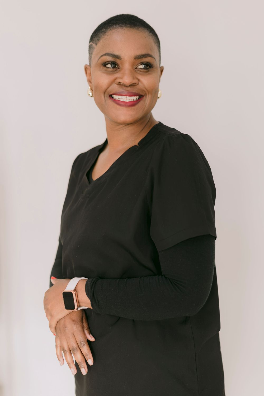 Smiling woman in black top with smartwatch poses confidently against light background.