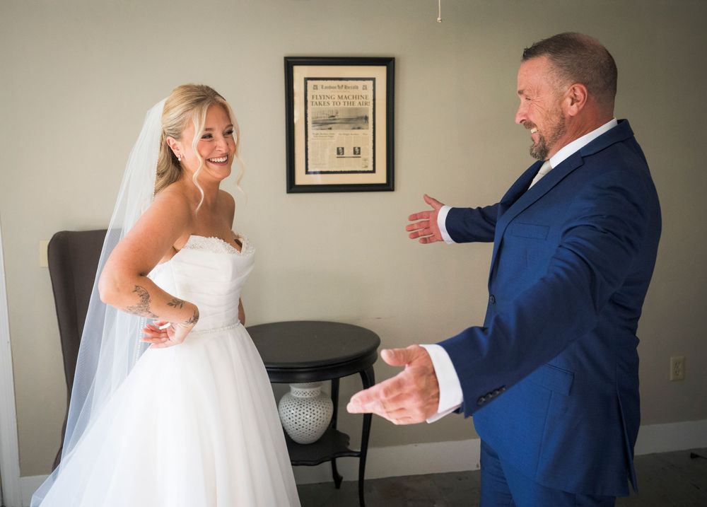 Groom in blue suit reacts with joy seeing bride in white wedding dress for the first time.