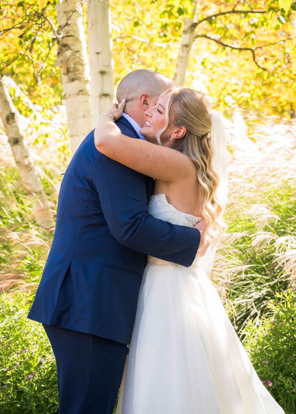 Bride and groom sharing a romantic embrace among golden autumn aspen trees outdoors.