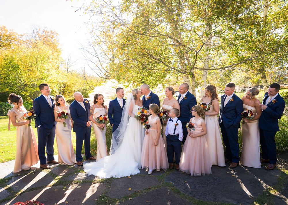 Large wedding party in navy and blush attire gathered outdoors on sunny fall day.