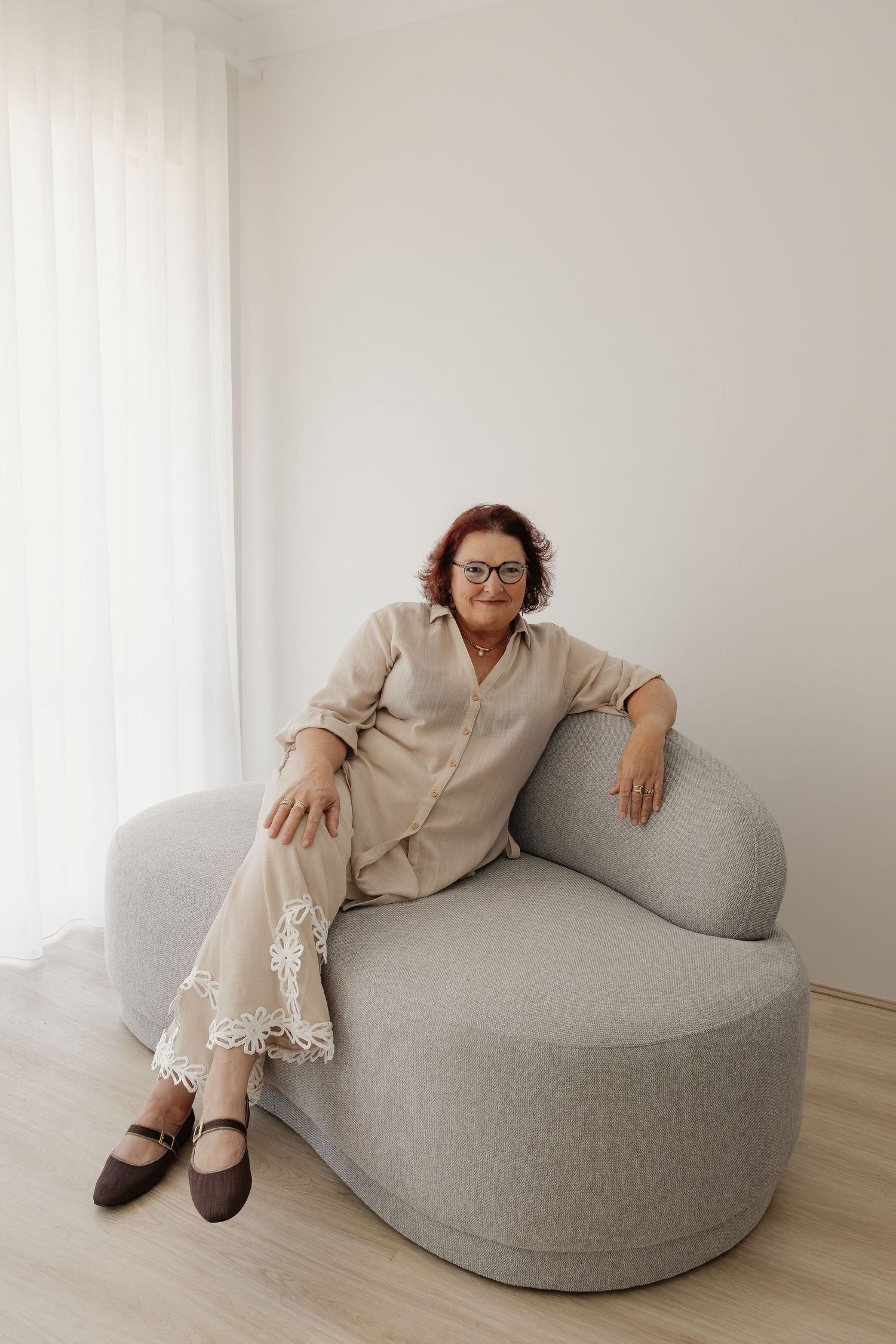 Woman relaxes in a curved armchair at a natural light studio in Wannanup, wearing a neutral linen outfit in a family session.