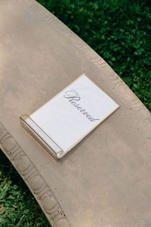 Elegant reserved sign card on a stone bench at an outdoor wedding ceremony.