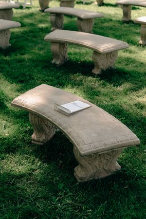 Ornate curved stone benches arranged on lush green grass, with a book resting on the nearest bench.