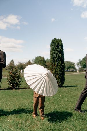 Person holding a white parasol umbrella on green grass at an outdoor wedding ceremony on a sunny day.