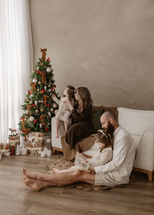 Family gathered around a decorated Christmas tree in a cozy living room, with children and parents sharing a festive holiday moment.