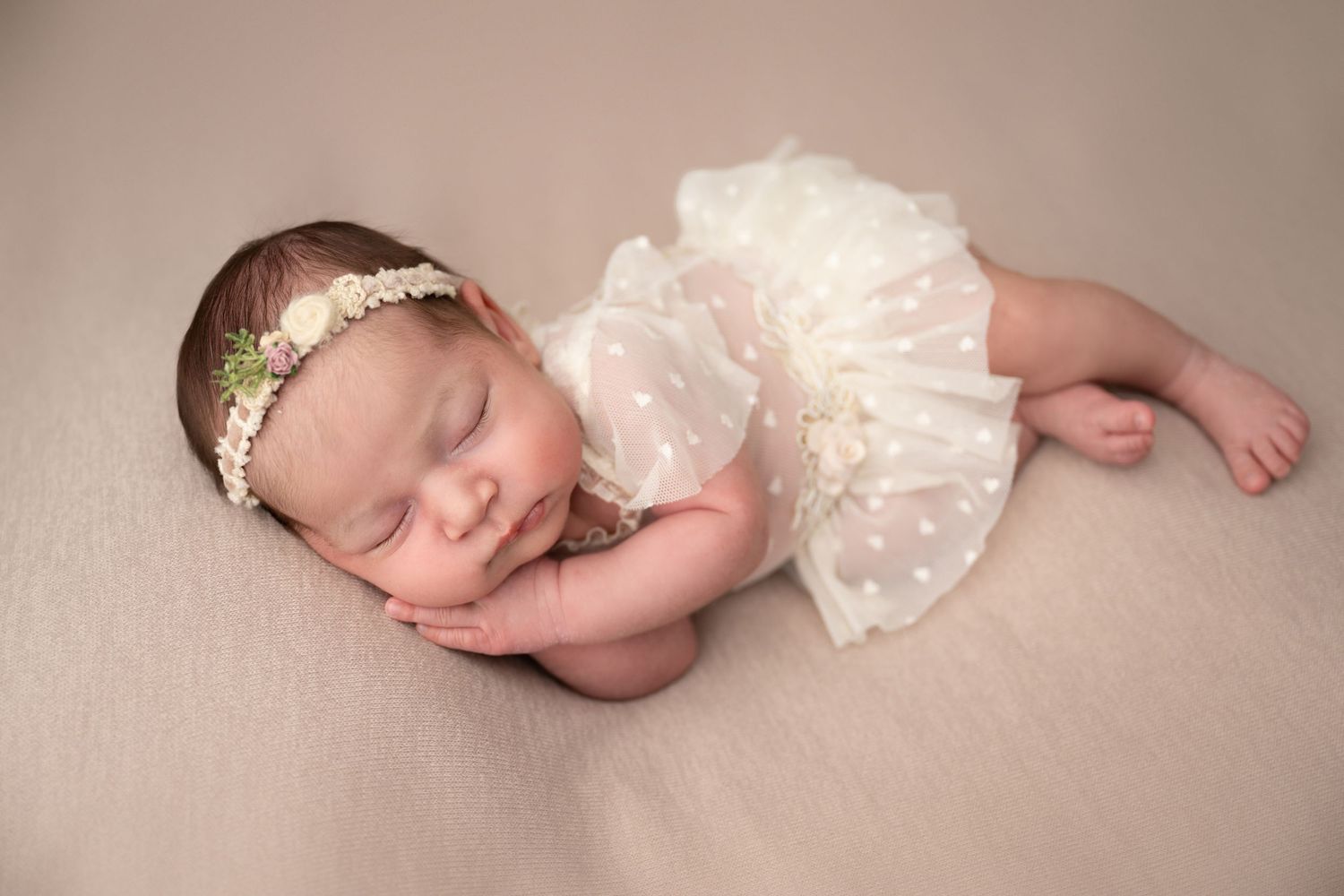 Sleeping newborn baby in a delicate white outfit during a posed studio newborn photography session in Linden, New Jersey.