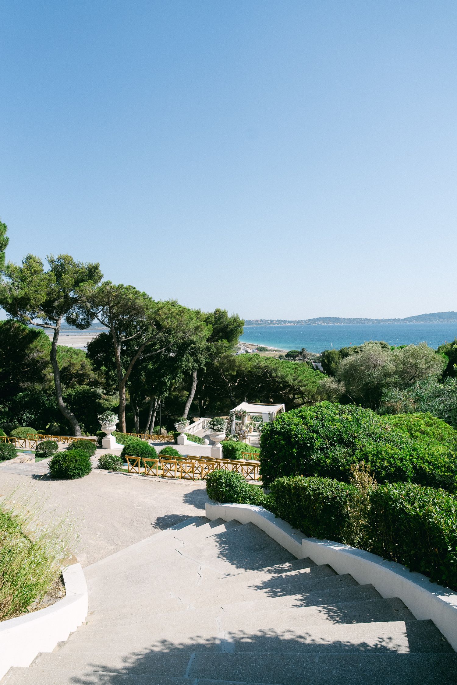 Scenic Mediterranean garden with lush greenery, white stone steps, and a stunning sea view under a clear blue sky.