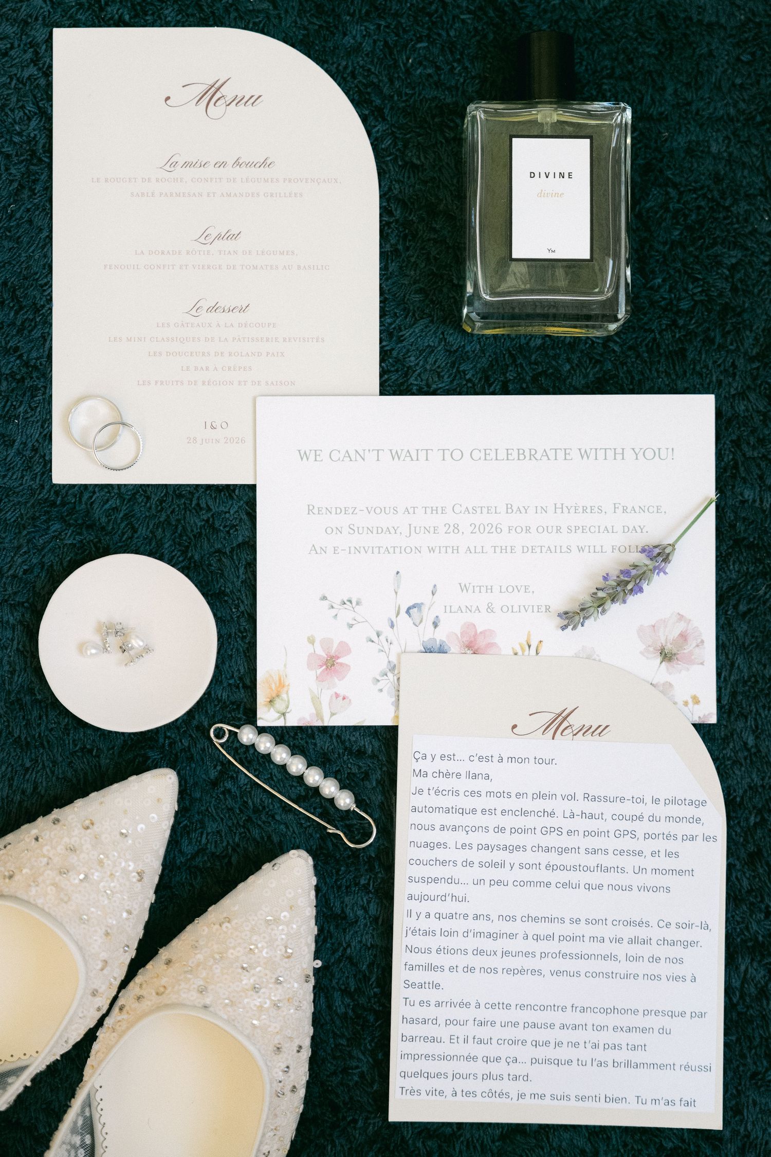 Elegant wedding flat lay with menu cards, floral invitations, pearl jewelry, lace heels, and a perfume bottle on green velvet.