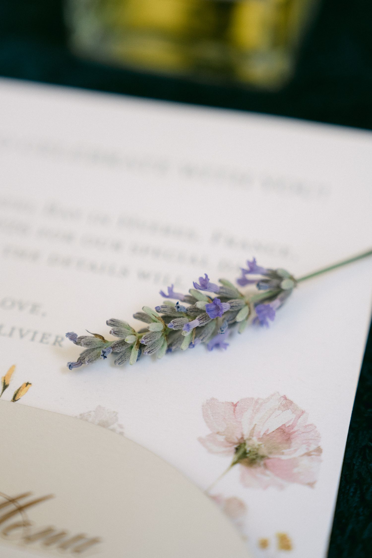 A sprig of fresh lavender resting on a floral wedding stationery card with pressed flower details.
