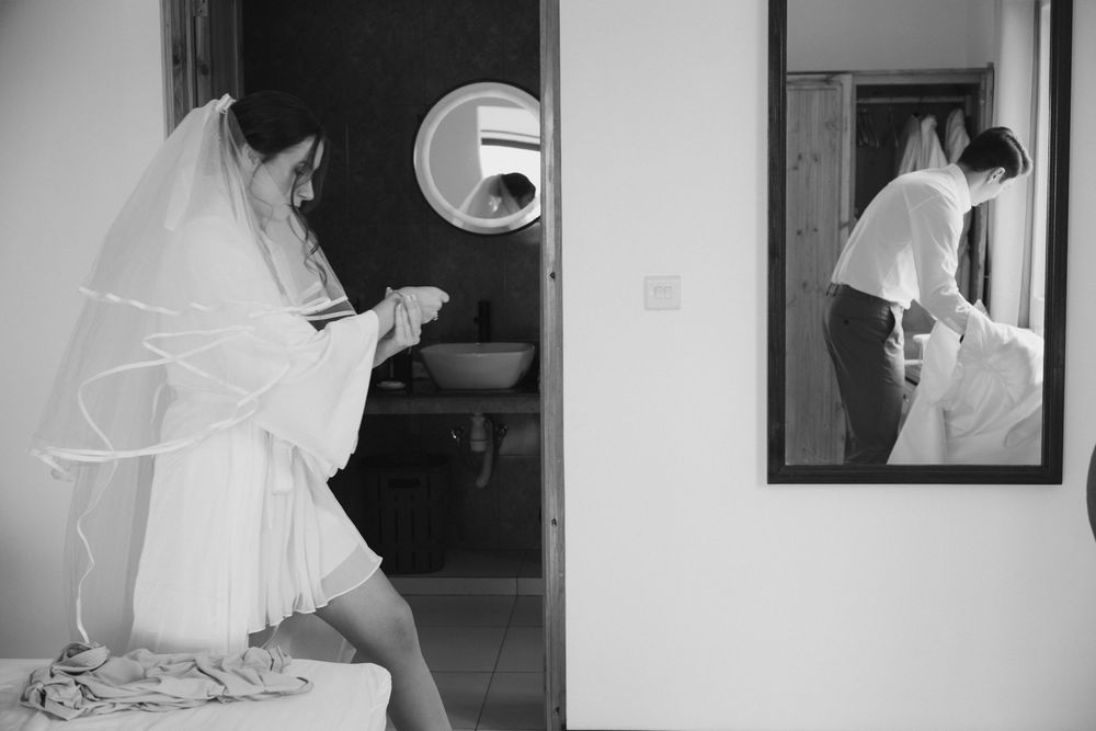 Black and white photo of a bride in a veil reading a note while her reflection shows in a mirror.