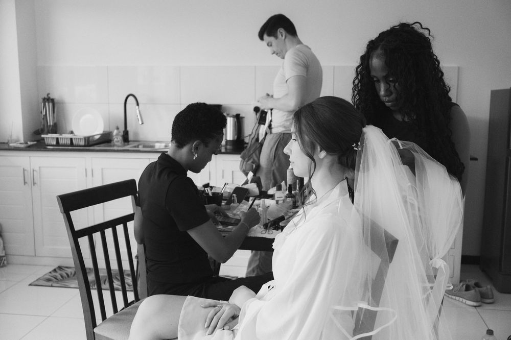 Black and white photo of a bride getting ready with wedding veil, assisted by stylists in a bright room.
