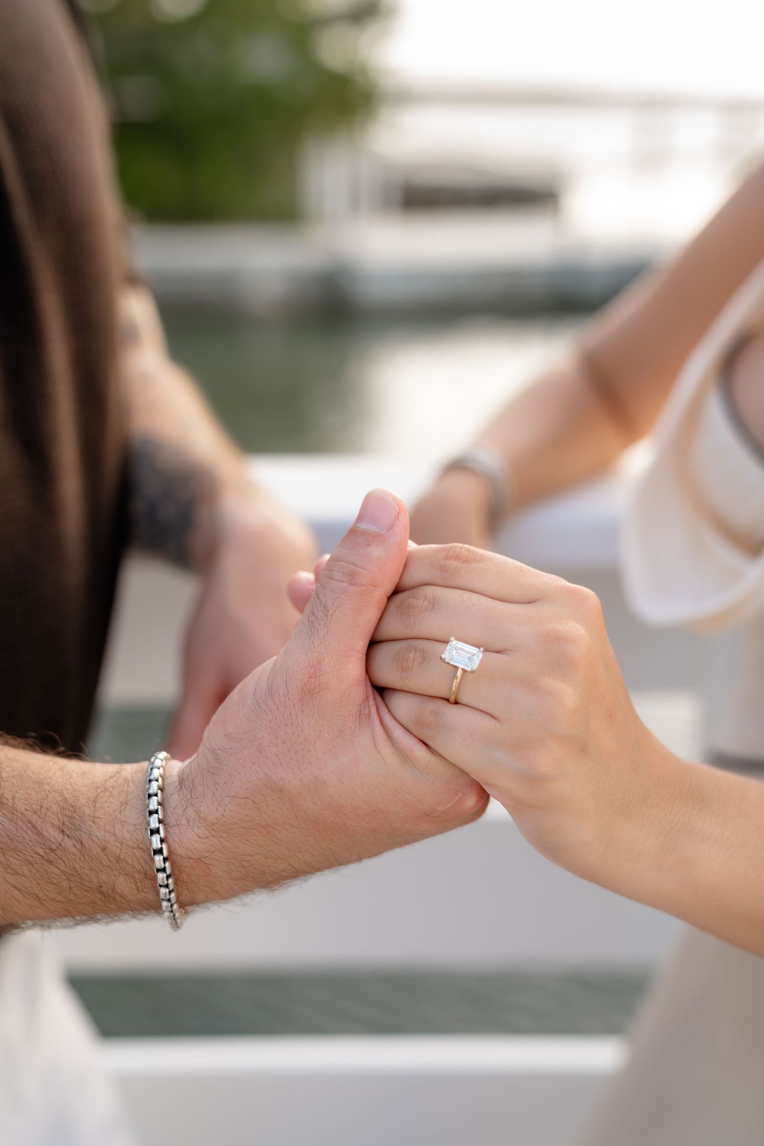 Close-up of couple holding hands showcasing a stunning emerald-cut diamond engagement ring on gold band.